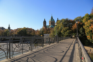 München: Brücke über die Isar mit der Kirche Sankt Lukas im Hintergrund im Herbst