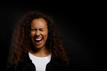 Portrait of young beautiful black woman standing in the dark showing emotions. Female with emotional facial expression over black wall background. Close up, copy space.