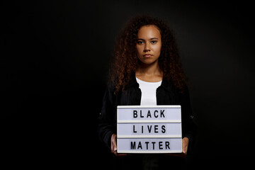 Portrait of young beautiful black woman standing in the dark with anti racist slogan. Protesting...