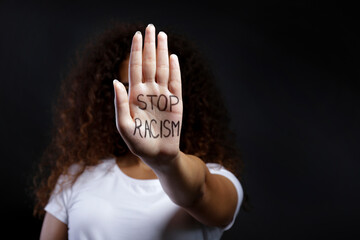 Portrait of young beautiful black woman showing a stop racism slogan written on palm of her hand....