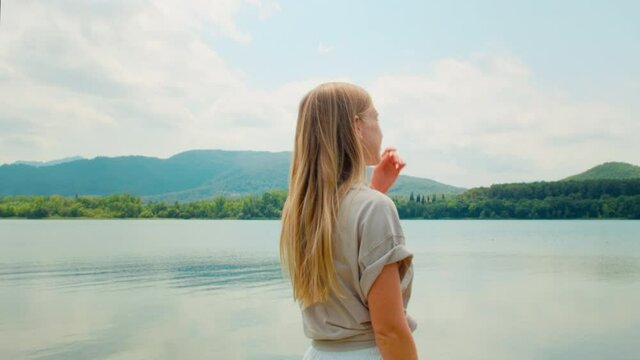 Simple and authentic young woman in casual clothes with long blonde hair looks around over amazing natural reserve in national park, mountain lake. Explore outdoors, travel influencer blogger