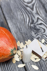 Orange pumpkin, seeds and candle stub. Beside a box of matches. On brushed pine boards painted black and white.