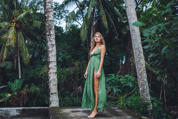 Woman in stylish gown looking at camera at exotic forest