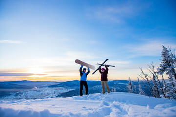 Two active friends snowboarder and skier standing on mountain top blue sky sunrise. Concept ski...