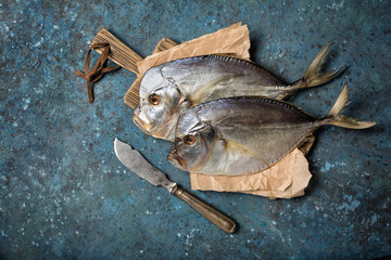 Two whole salty vomer fish on wooden board with vintage knife