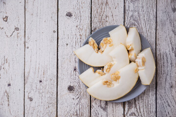 
melon, slices of juicy melon with seeds in a plate on a light wooden table with place for copy space. Oval Uzbek Russian Melon
