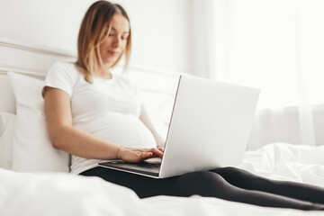 Pregnant freelancer using laptop on bed