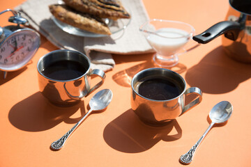 Morning Breakfast-coffee in metal cups, milk, rolls, orange background, sun glare and shadows....