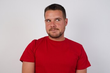 Fototapeta premium Photo of amazed Young caucasian man wearing red t-shirt over white background bitting lip and looking up to empty space,