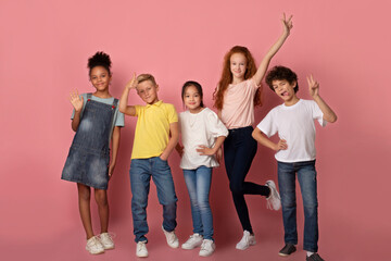 Joyful schoolkids making faces and showing variety of gestures over pink background, full length portrait