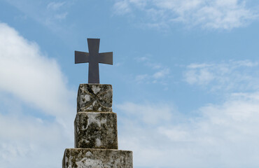 Beautiful photo of holy cross fixed on top of old and dusty cement pillar with clear blue sky and sparse white clouds in background. Concept of haunting, exorcism, belief, church, jesus, cemetery etc.