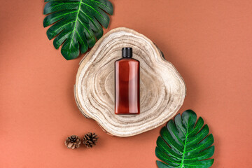 Brown bottle of lotion, cream, shampoo on wooden cross section cut with monstera leaves on brown...