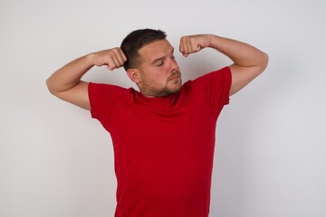 Young caucasian man wearing red t-shirt over white background showing arms muscles smiling proud. Fitness concept.