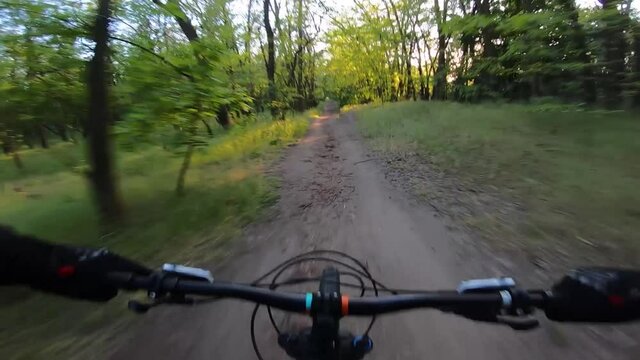 The cyclist rides along a rocky trail on sunset FPV. First-person view.
