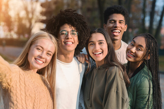 Positive multiracial teen friends taking selfie while walking in park
