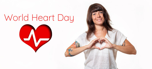 A woman with tattoos shows a heart sign with her hands and smiles. White background. Drawing of a heart with a cardiogram. The concept of world heart day