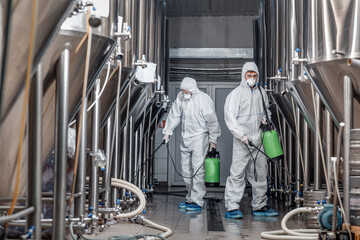 Worker in hazmat suit making disinfection inside beer plant
