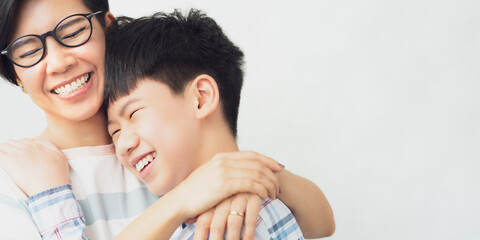 Portrait of stylish middle aged Asian mother and smart looking preteen son hug, smile and laugh...