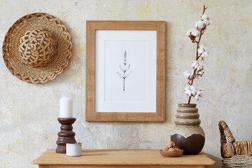 Stylish boho interior of living room with brown mock up poster frame, elegant accessories, flowers...
