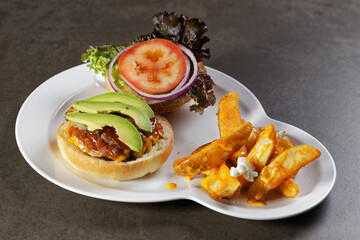 Juicy beef burger with cheese, bacon, tomato, lettuce, dressings, avocado, red onion and accompanied by french fries.