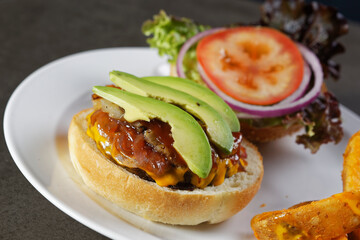 Juicy beef burger with cheese, bacon, tomato, lettuce, dressings, avocado, red onion and accompanied by french fries.