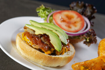 Juicy beef burger with cheese, bacon, tomato, lettuce, dressings, avocado, red onion and accompanied by french fries.