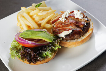 Juicy beef burger with cheese, bacon, tomato, lettuce, dressings, avocado, red onion and accompanied by french fries.