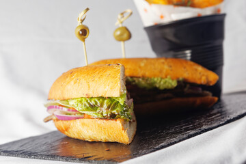 Beef baguette with tomato, lettuce, avocado and dressings accompanied by french fries.