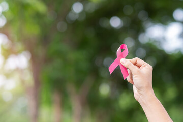 October Breast Cancer Awareness month, adult Woman  hand holding Pink Ribbon with green background for supporting people living and illness. International Women, Mother and World cancer day concept