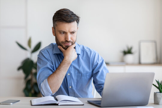 Thoughtful Businessman Working With Computer In Office, Looking At Laptop Screen