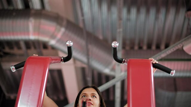 Sporty young woman doing pull ups in gym. Low angle view of athletic focused young woman in sportswear exercising and looking aside in gym