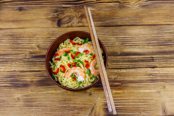 Bowl of instant Chinese noodles with shrimps, green onion and red hot chilli peppers on wooden table. Top view