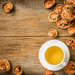 Top view of bael tea in white cup on white saucer with dry bael on wooden background.