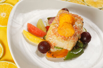 Roasted tilapia fish fillet with pumpkin, bell pepper, carrot, and orange, grapefruit, and lemon wedges.