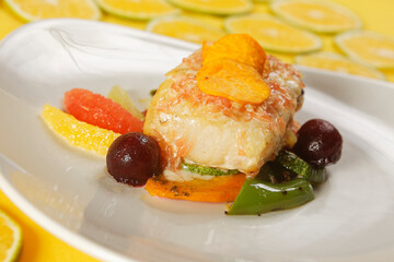 Roasted tilapia fish fillet with pumpkin, bell pepper, carrot, and orange, grapefruit, and lemon wedges.