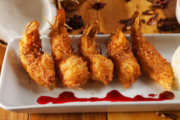 Breaded shrimp with Coconut shell in Jamaican sauce, accompanied by steamed rice and garnished with pumpkin and carrot vegetables.