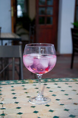 Copa de Gin Tonic Rosa con grosellas sobre una mesa con baldosas hidráulicas
