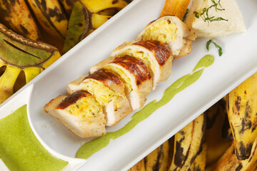 Sliced Suprem chicken and stuffed with plantain accompanied by green sauce and steamed rice.