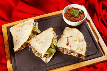 Traditional Oaxacan tlayuda stuffed with meat, melted cheese and avocado, accompanied by red chili sauce.