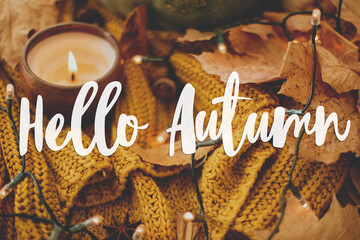 Hello autumn, hand written  text on background of pumpkin, autumn leaves, candle, warm lights on...