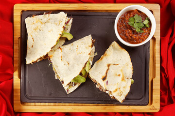 Traditional Oaxacan tlayuda stuffed with meat, melted cheese and avocado, accompanied by red chili sauce.