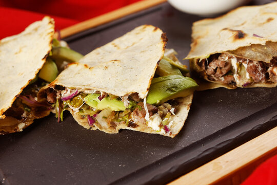 Traditional Oaxacan tlayuda stuffed with meat, melted cheese and avocado, accompanied by red chili sauce.