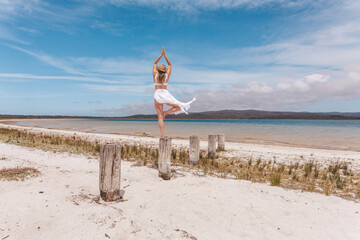 Beautiful woman balance on wooden post yoga pose in swimwear and sarong