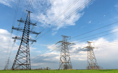 Pylons of electrical net on a panorama of blue cloudy sky and green meadow