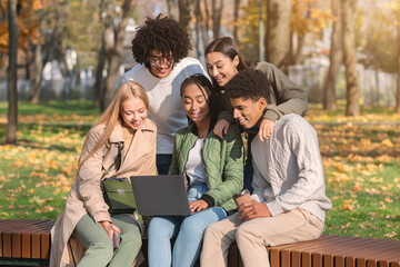 Carefree multiethnic teenagers using laptop in park
