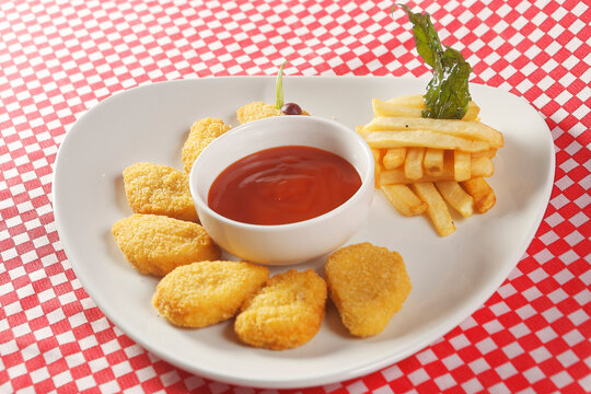 Chicken nuggets with ketchup served with french fries.