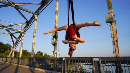 Beautiful sports girl aerialist. circus acrobat on aerial straps, metallic trusses of the bridge....