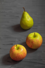 Two ripe apples and one pear on a dark gray background