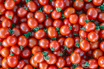 Raw market fresh cherry tomato background with multiple tomatoes lying on the market counter.