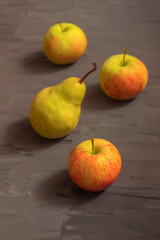 Three fresh fruit with an apple tree and one yellow pear on a dark gray background